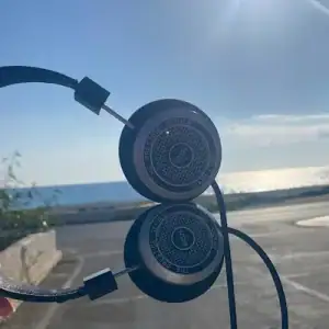 The headphones are held to the left of the shot - at 90 degrees with a sea background.