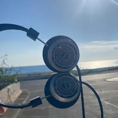 The headphones are held to the left of the shot - at 90 degrees with a sea background.